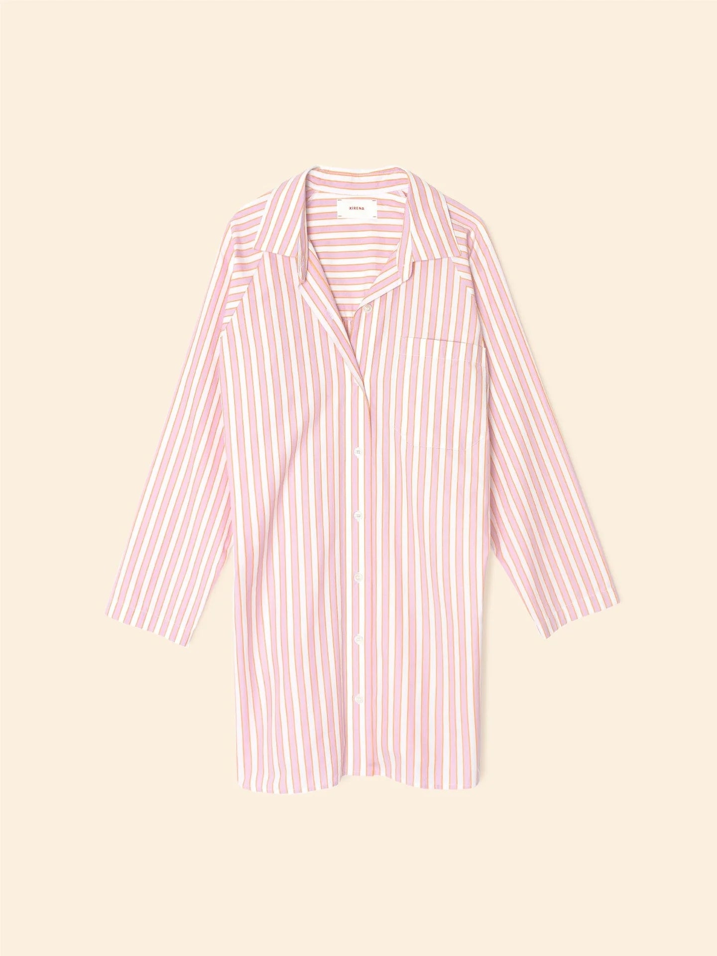 Introducing the Flora Dress by Xirena: A pink and white vertically striped button-up dress with long sleeves and a collar, crafted from 100% cotton. This elegant piece is perfect for any occasion, displayed beautifully on a plain beige background.