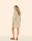 A person with curly hair wears a Flora Dress by Xirena and sandals, facing away. The 100% cotton dress showcases vertical white and brown stripes on a light beige background.