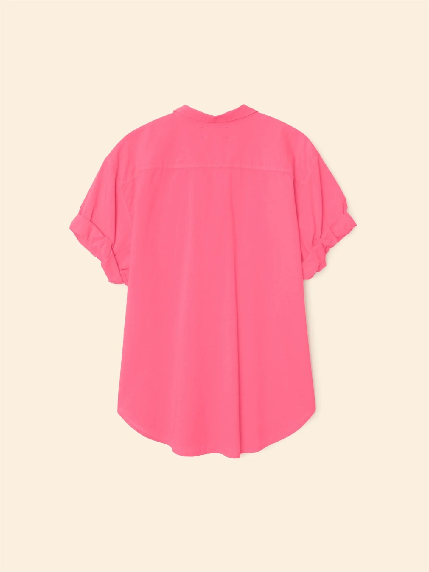 The Xirena Channing Shirt S25 in bright pink cotton chambray is shown from the back on a beige background, featuring rolled cuffs, a curved hem, and a hint of &quot;boy meets girl&quot; style.