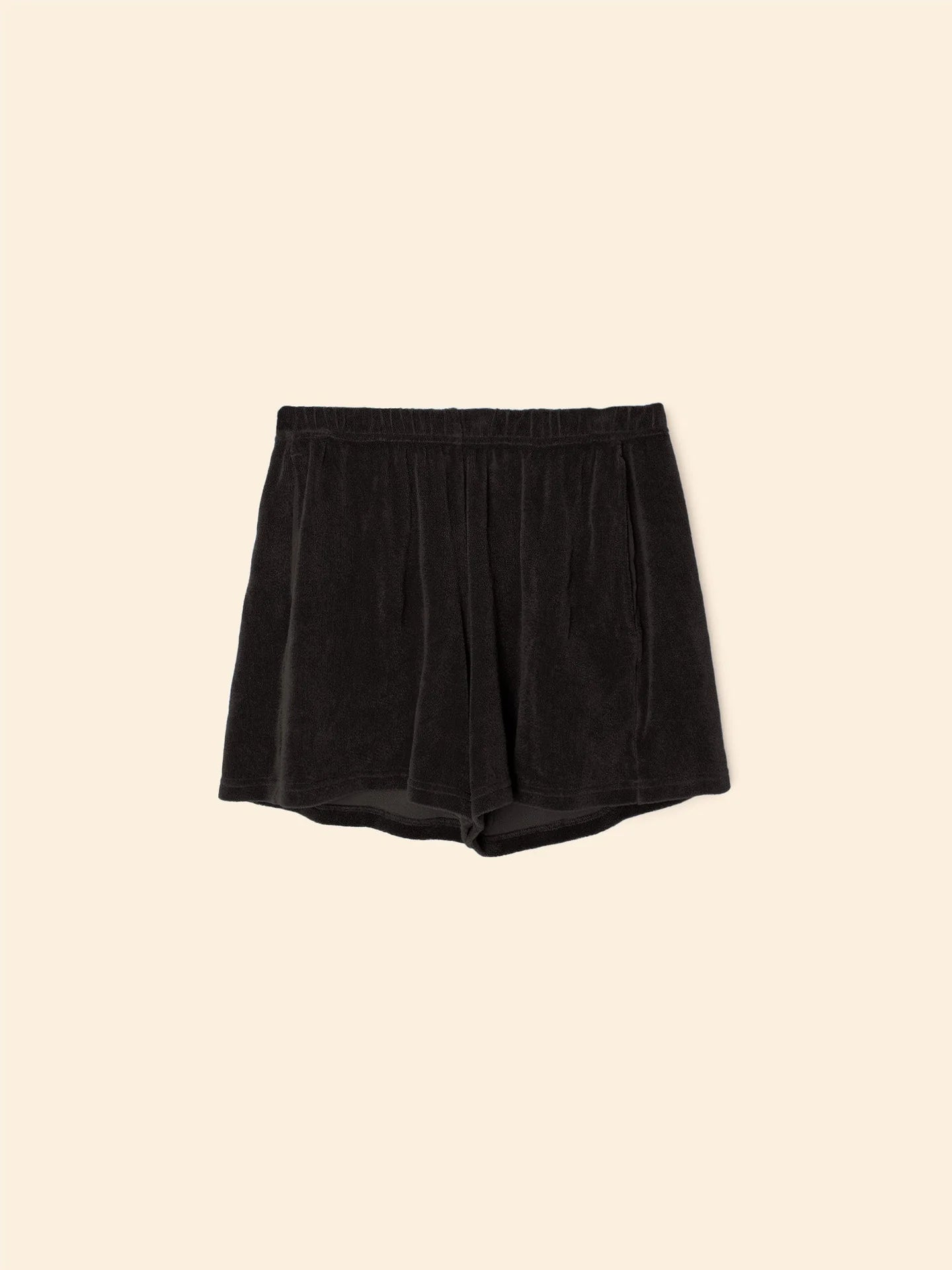 The Shayden Short by Xirena is a black terry cotton-blend sweat short with an elasticized waist, shown flat on a plain beige background.