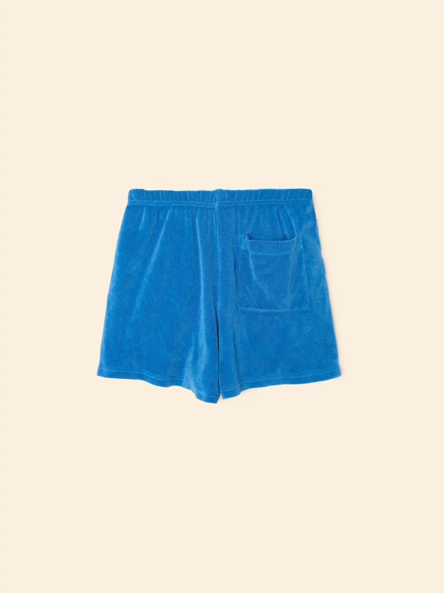 The Shayden Short by Xirena is a bright blue cotton-blend sweat short with an elastic waist and a single square front pocket, shown on a plain beige background.