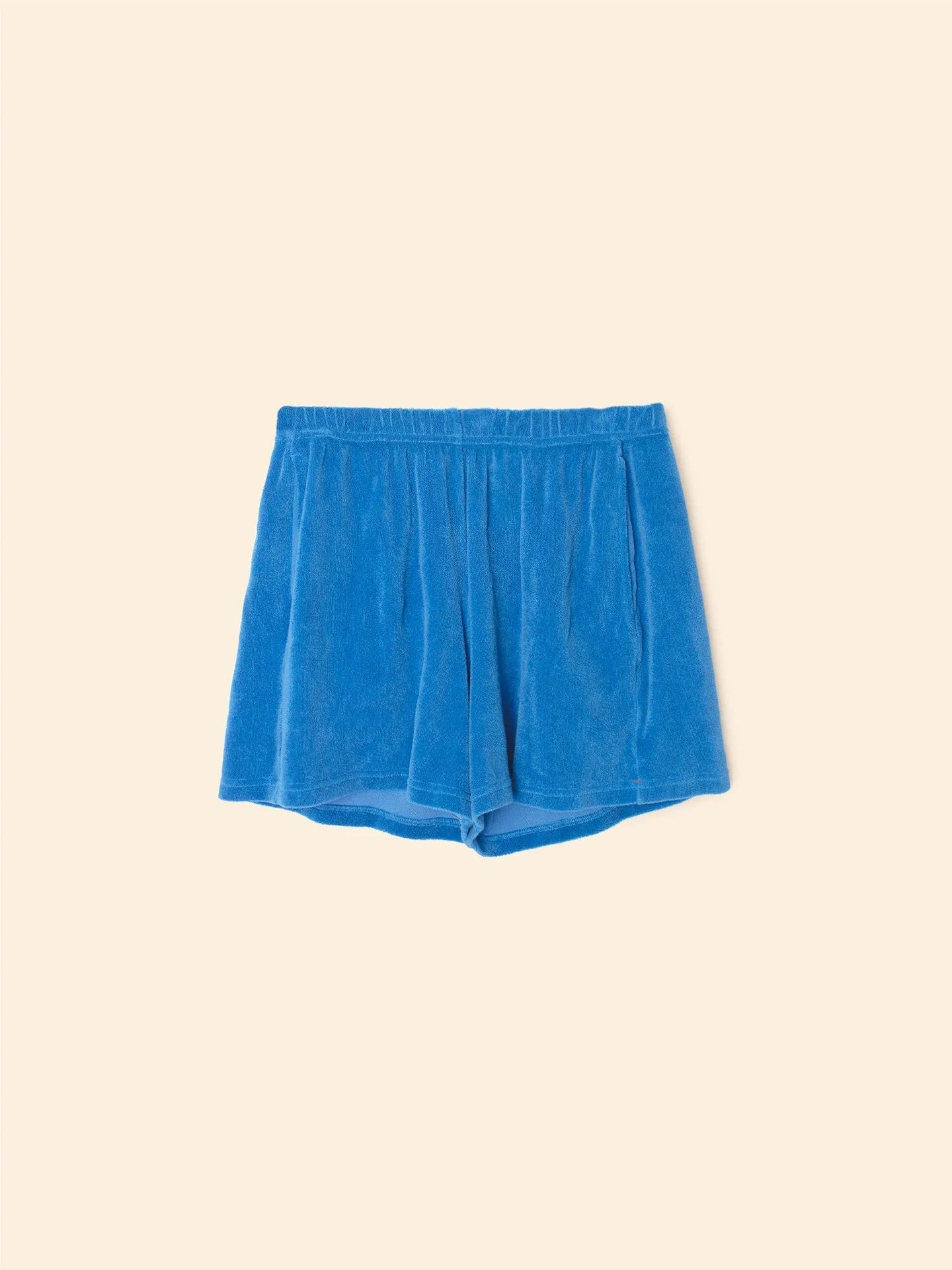 The Shayden Short by Xirena features a bright blue hue in a soft cotton blend with an elastic waist, shown flat on a beige background.