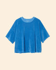The Roe Top by Xirena is a loose-fitting, short-sleeved blue velour T-shirt featuring a darker blue crew neckline, made from a soft cotton blend, shown on a plain beige background.