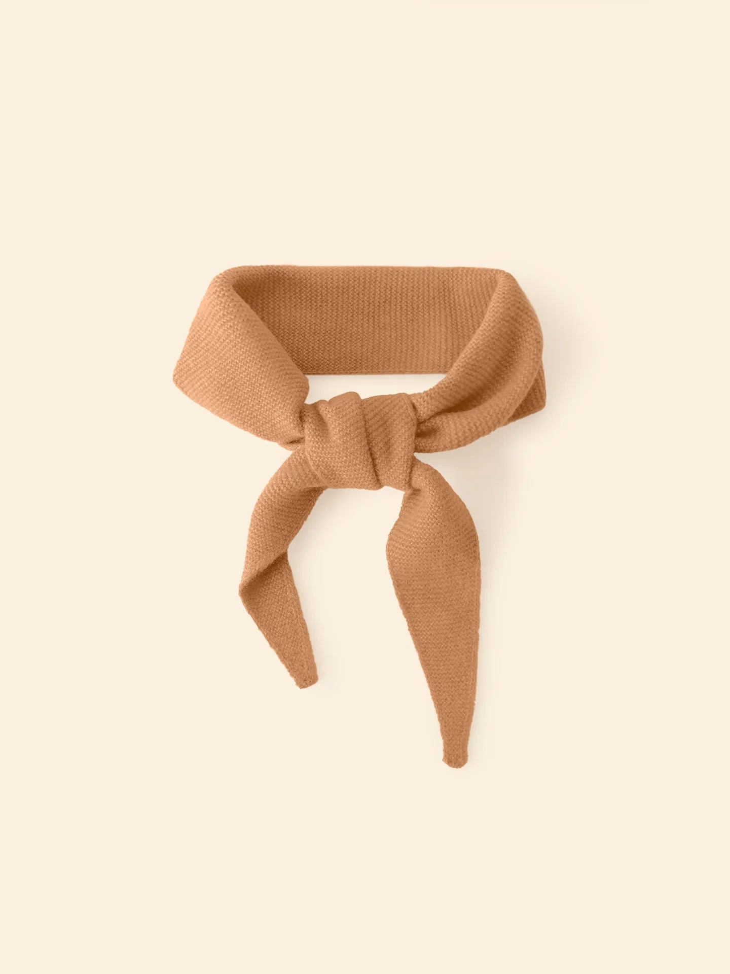 The Xirena Myla Scarf, an ultra-soft light brown cashmere accessory with two pointed ends, is shown tied in a loose knot against a cream backdrop.
