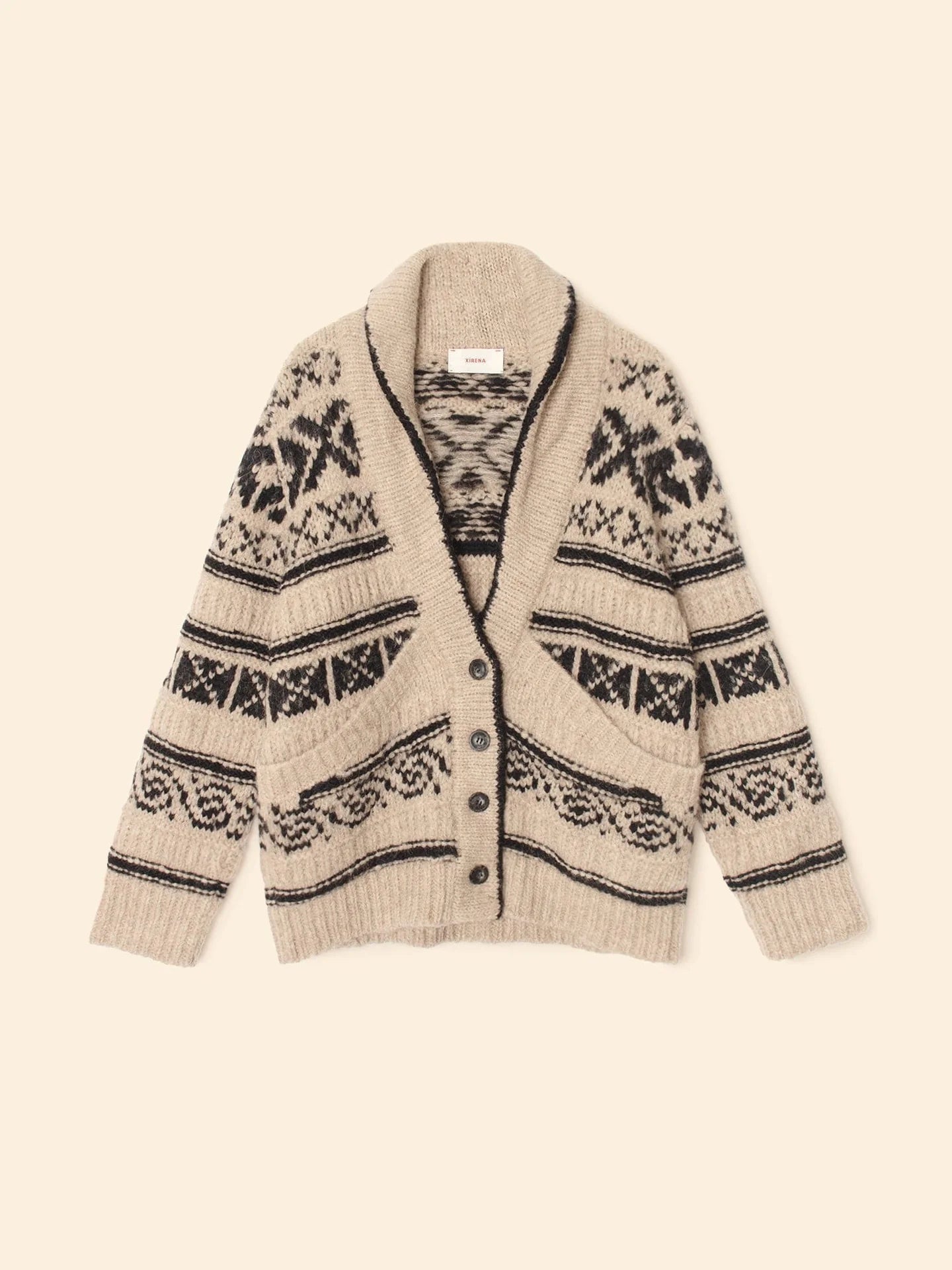 The Xirena Vail Cardigan, a beige alpaca sweater with black geometric and snowflake patterns, shawl collar, front buttons, and two pockets, is displayed flat on a cream background.