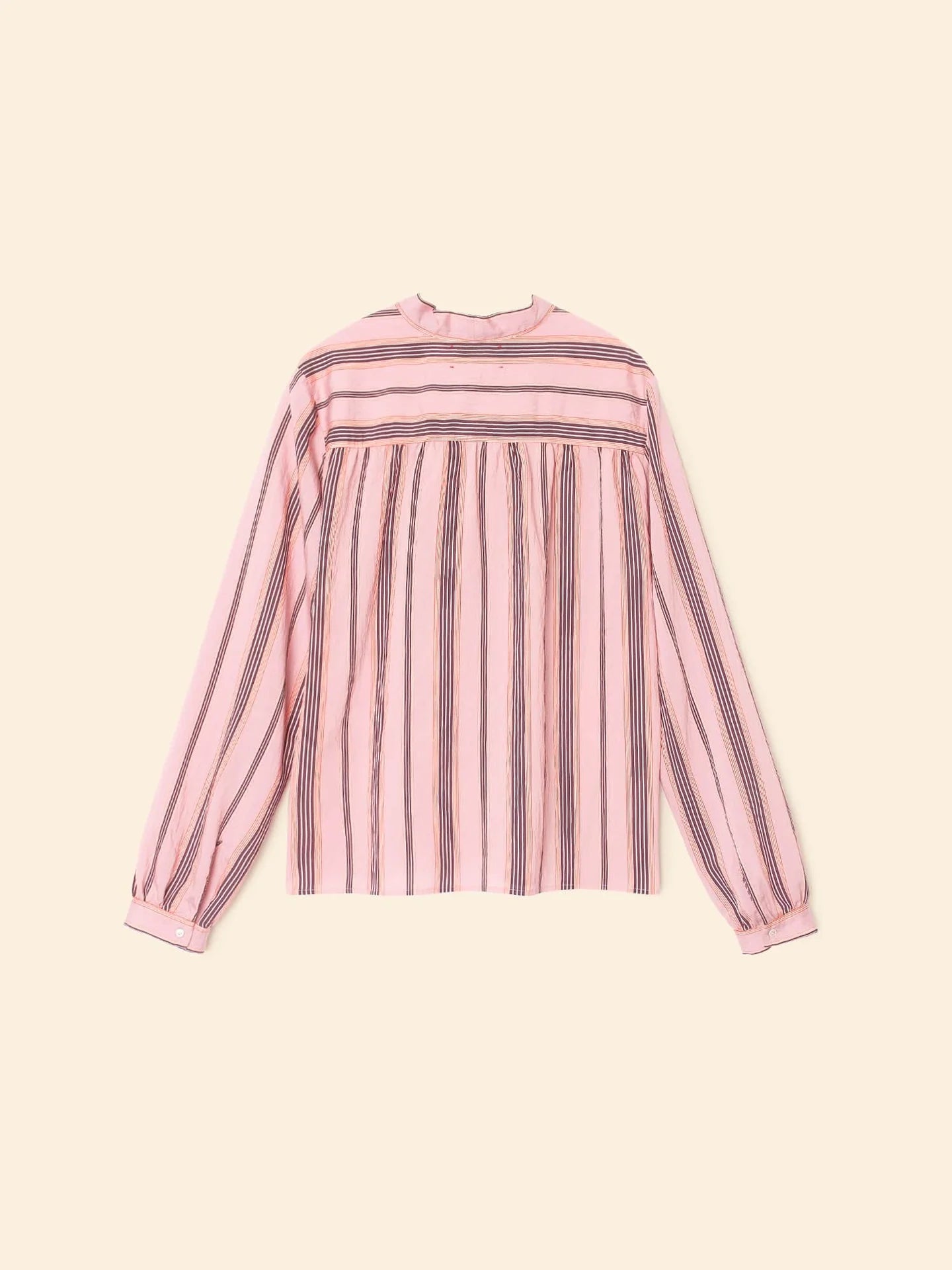 The Sabina Top by Xirena is a long-sleeved pink striped blouse with dark vertical and horizontal patterns, crafted from drapey viscose. It features a high neckline and buttoned cuffs, shown against a plain beige background.