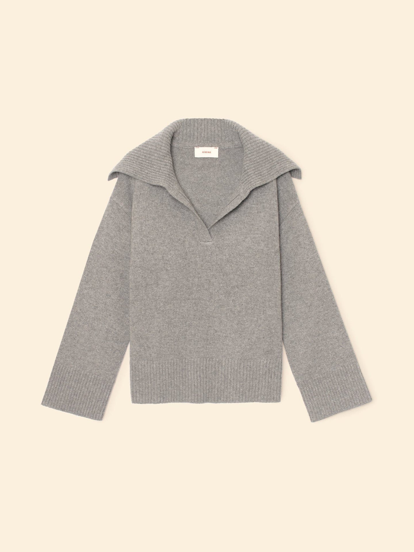 The Xirena Mattia Sweater is a light gray, long-sleeve cashmere pullover with a wide collar and deep V-neck. Displayed flat on a beige background, it features ribbed cuffs and hem for added style.