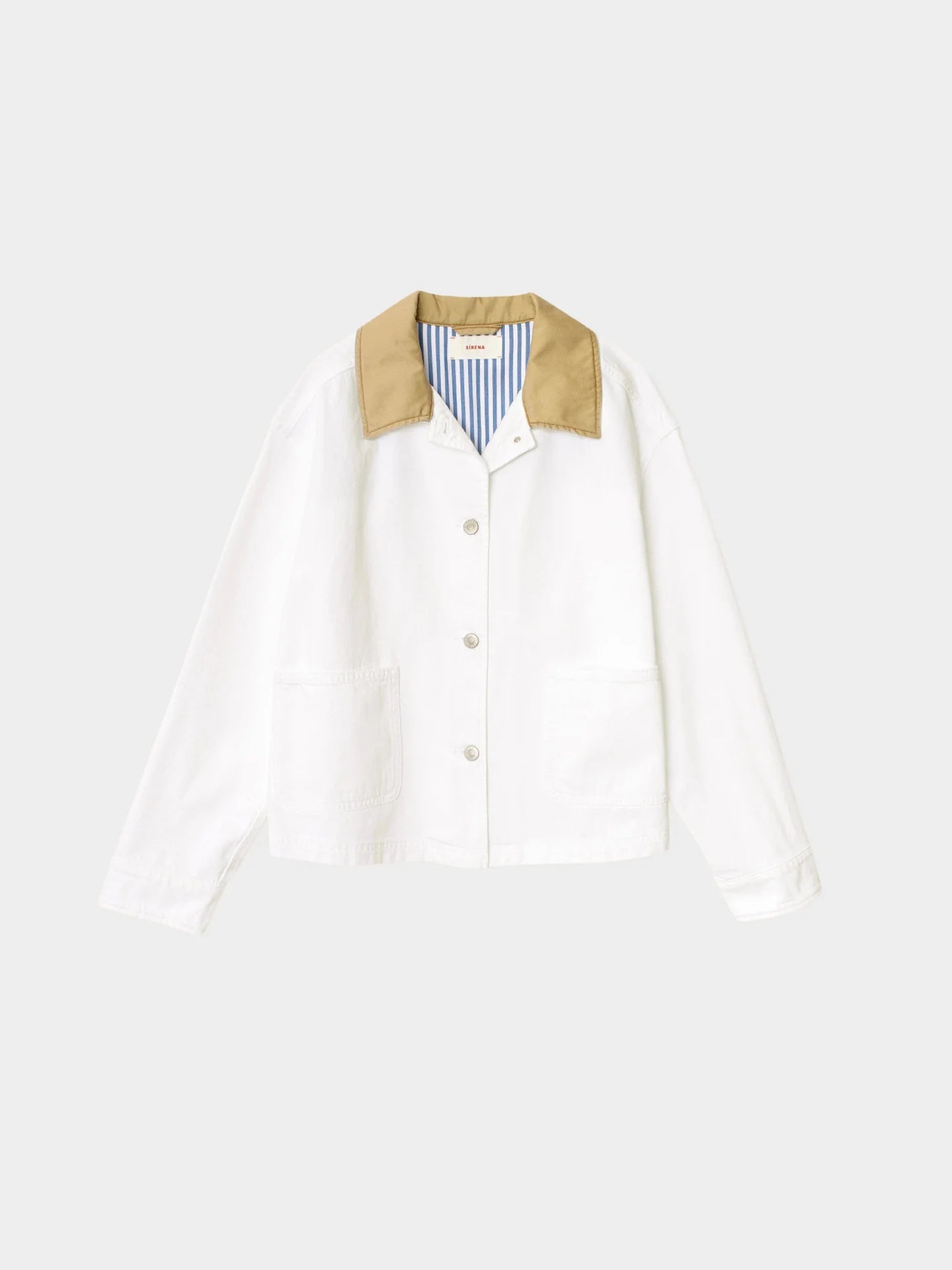 The Xirena Cove Jacket is a lightweight white denim button-up with large front pockets, a tan collar, and blue-and-white striped lining, shown against a plain light gray background.