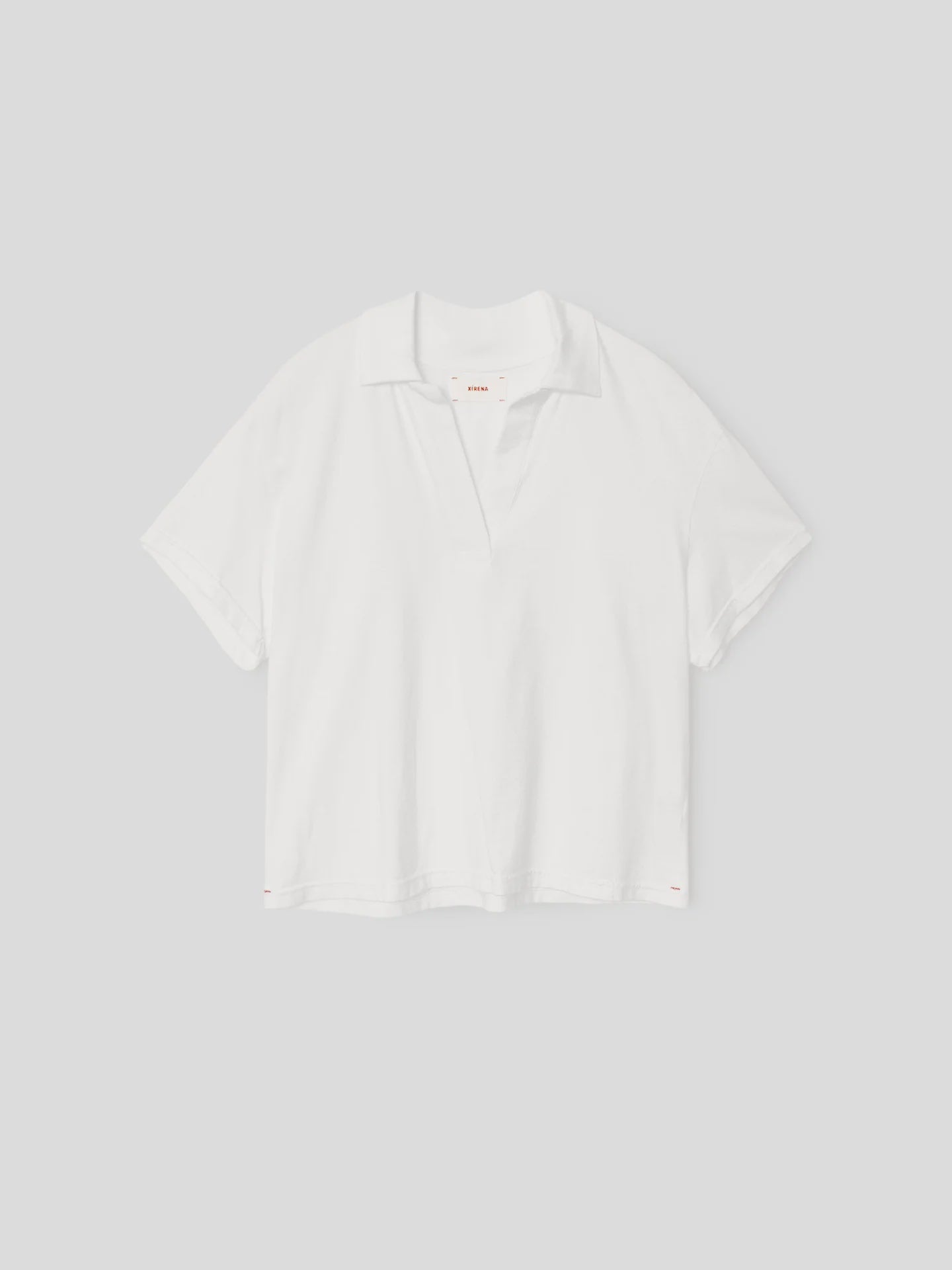 The Spencer Tee by Xirena is a relaxed-fit, plain white cotton polo with short sleeves and an open V-neck collar, made in Los Angeles and shown on a light gray background.