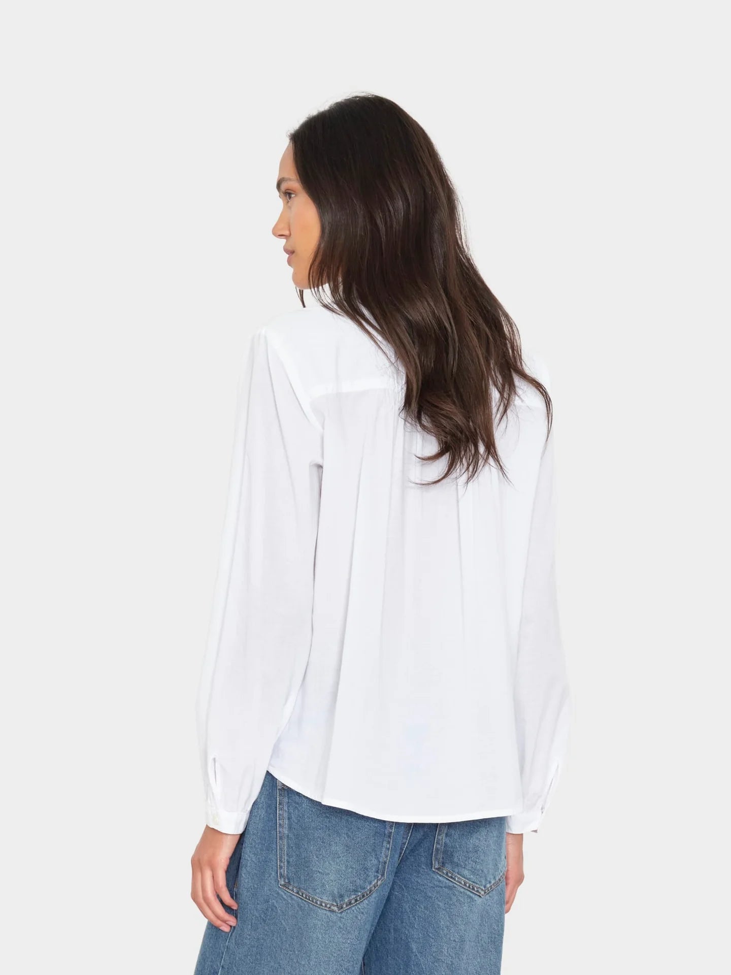 Xirena Amanda Shirt in white on woman with long brown hair, paired with blue jeans, back view.