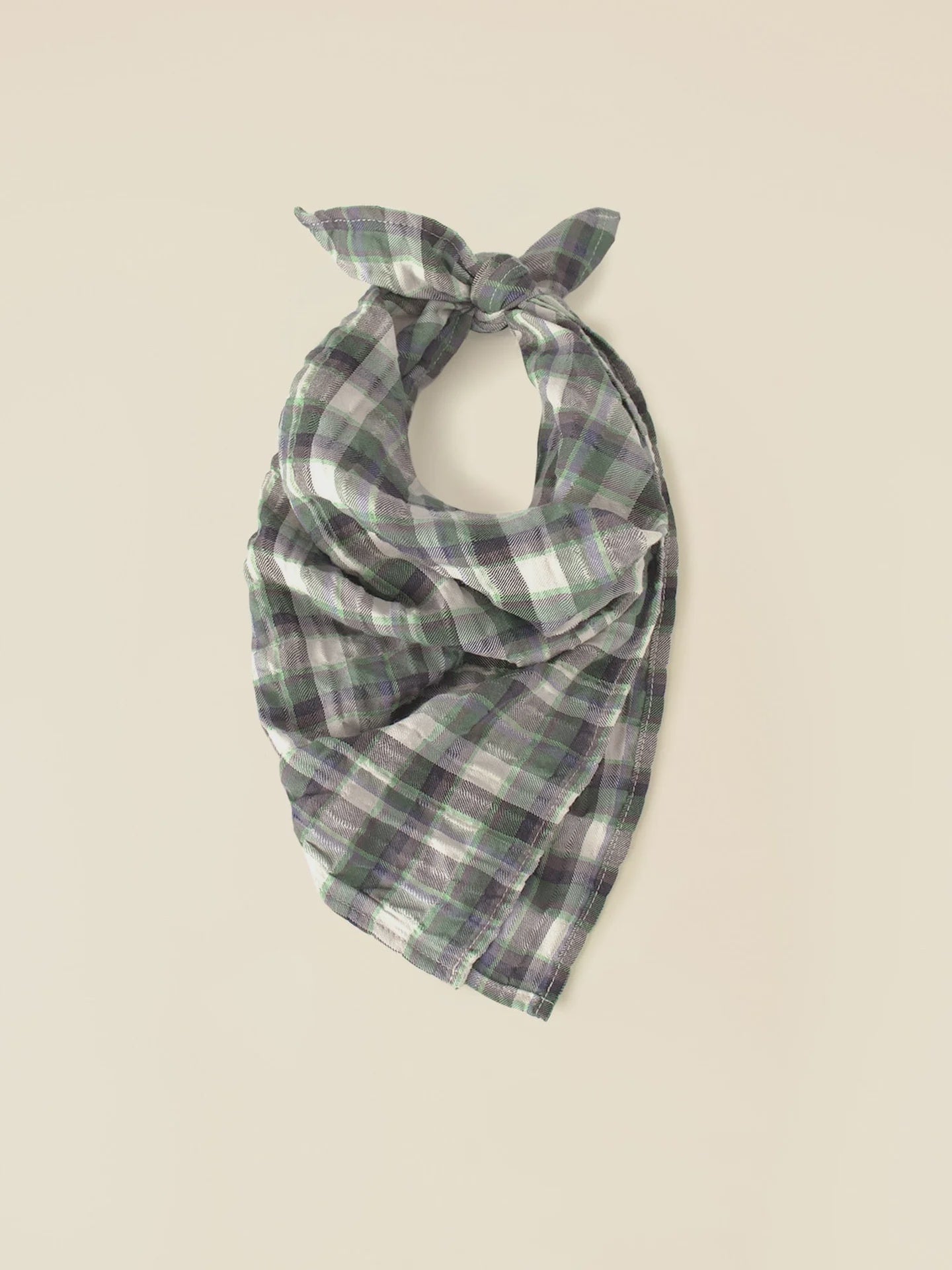 The Xirena Bandana, a versatile piece in green, gray, and white crinkled double plaid, is fashioned into a neat knot at the top and displayed on a plain, light background.