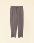 The Draper Pant Ash by Xirena is a pair of gray high-waisted pull-on pants with a drawstring waist, made from soft cotton poplin. They offer a wide, relaxed fit and are equipped with two side pockets, beautifully showcased on a plain beige background.