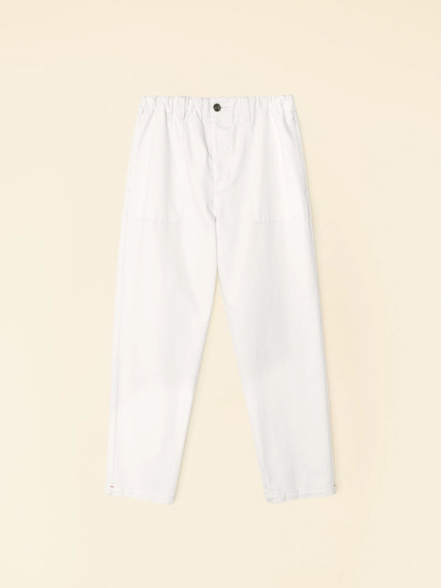 The Mercer Pant by Xirena is displayed on a light beige background, featuring white color with an elastic waistband and button fly. Crafted from recycled denim, these pants offer a relaxed fit with prominent seams on the front.