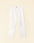 The Mercer Pant by Xirena is displayed on a light beige background, featuring white color with an elastic waistband and button fly. Crafted from recycled denim, these pants offer a relaxed fit with prominent seams on the front.