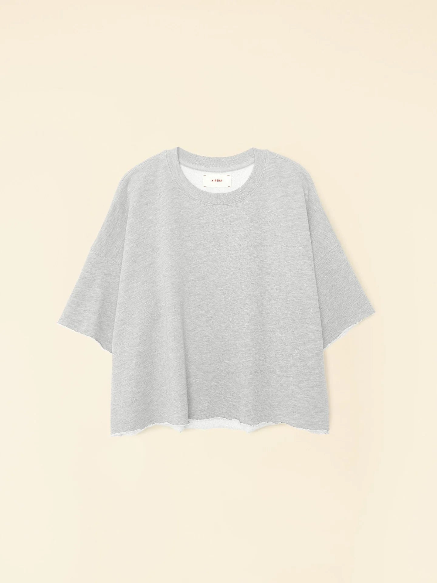 The Romeo Sweatshirt by Xirena, a gray, loose-fitting t-shirt with raw edge sleeves, is showcased on a light beige background. This sweatshirt features a round neckline and delivers elevated comfort with its casual, relaxed design.