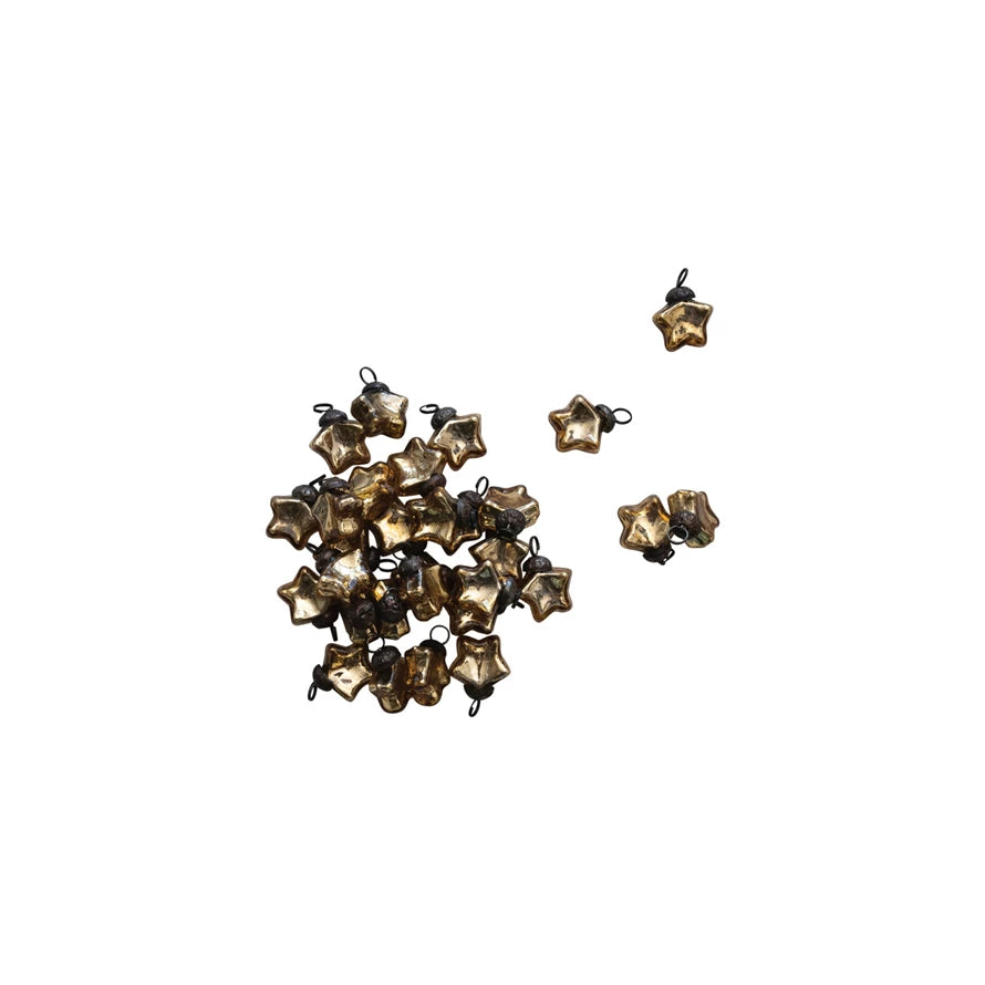 A cluster of Creative Co-op Mini Glass Star Ornaments with a gold finish and black loops are scattered on a white background. Four ornaments are separated, resembling delicate Christmas tree decorations.