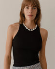 A woman with shoulder-length brown hair, wearing a Donni black sleeveless Rib Tank and a pearl necklace, stands against a neutral background in Scottsdale, Arizona.