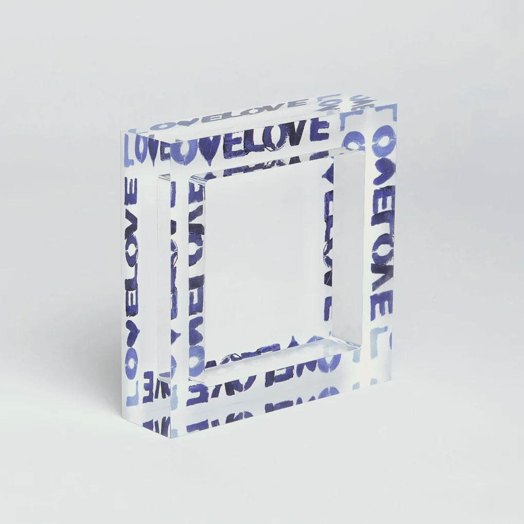 A Love on Repeat deco bowl by Kerri Rosenthal, with the word "LOVE" repeatedly printed in a blue, graffiti-style font. The cube is positioned against a plain white background reminiscent of an Arizona bungalow.