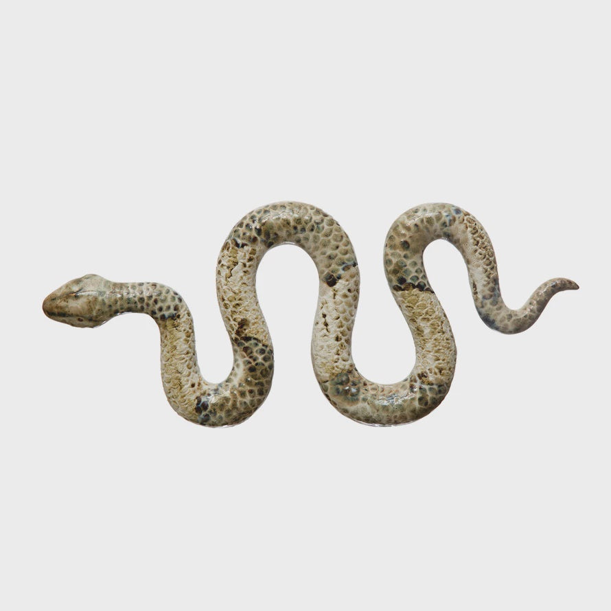 A realistic Stoneware Snake from Bloomingville, with a lifelike pattern, positioned in a sinuous shape against the plain white background of a Scottsdale, Arizona bungalow.