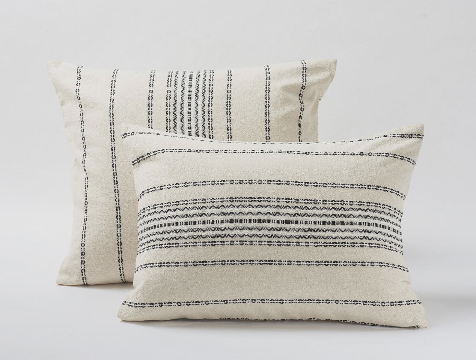 Two Rippled Black Stripe Euro Ivory pillows featuring intricate black and gray patterns on a cream background, set in a bungalow-style room with a light gray studio backdrop from Coyuchi Inc.